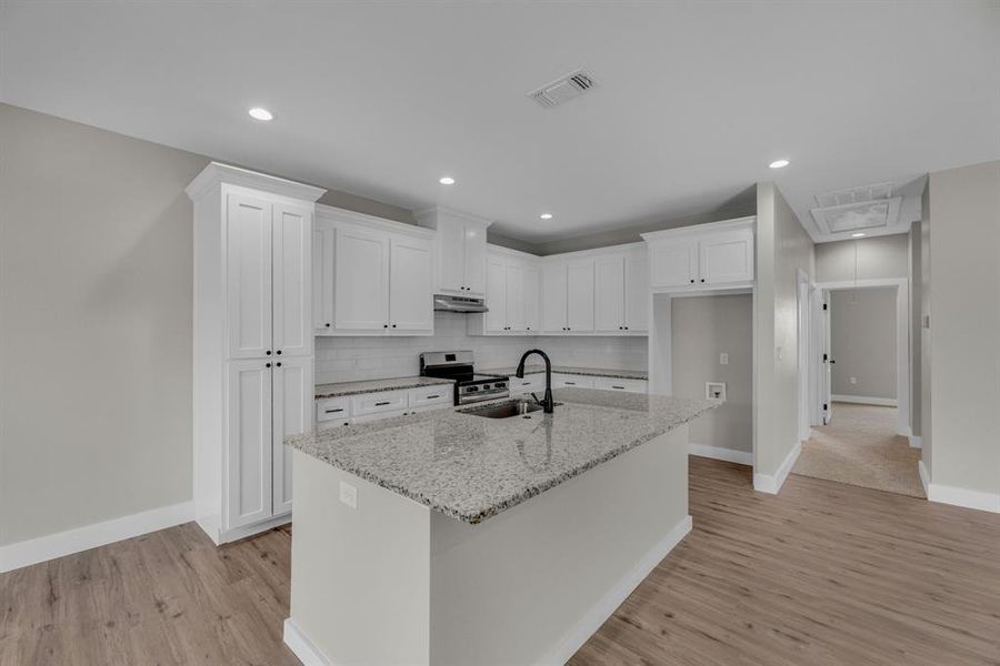 Kitchen with stainless steel electric range, a kitchen island with sink, light stone counters, light wood-type flooring, and white cabinets