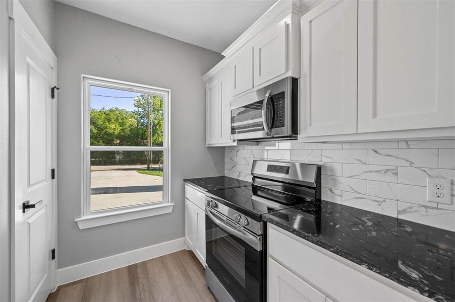 Kitchen with dark stone counters, light wood-type flooring, white cabinetry, stainless steel appliances, and backsplash