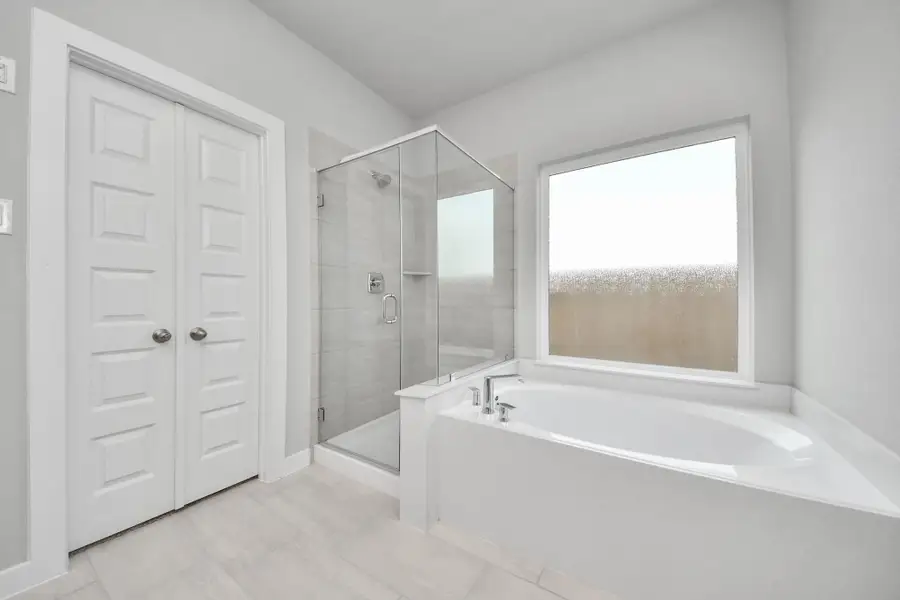 Indulge in a spa-like retreat within the confines of this primary bathroom. Delight in a spacious walk-in shower enveloped in stylish tile surround, unwind in a separate garden tub adorned with custom detailing. Sample photo of completed home with similar floor plan. Actual colors and selections may vary.