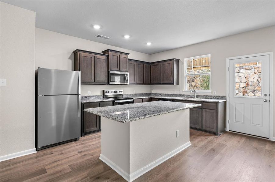 Kitchen with stainless steel appliances, dark brown cabinetry, light stone countertops, light wood-style floors, and a kitchen island Kitchen with stainless steel appliances, dark brown cabinetry, light stone countertops, light wood-style floors, and a kitchen island