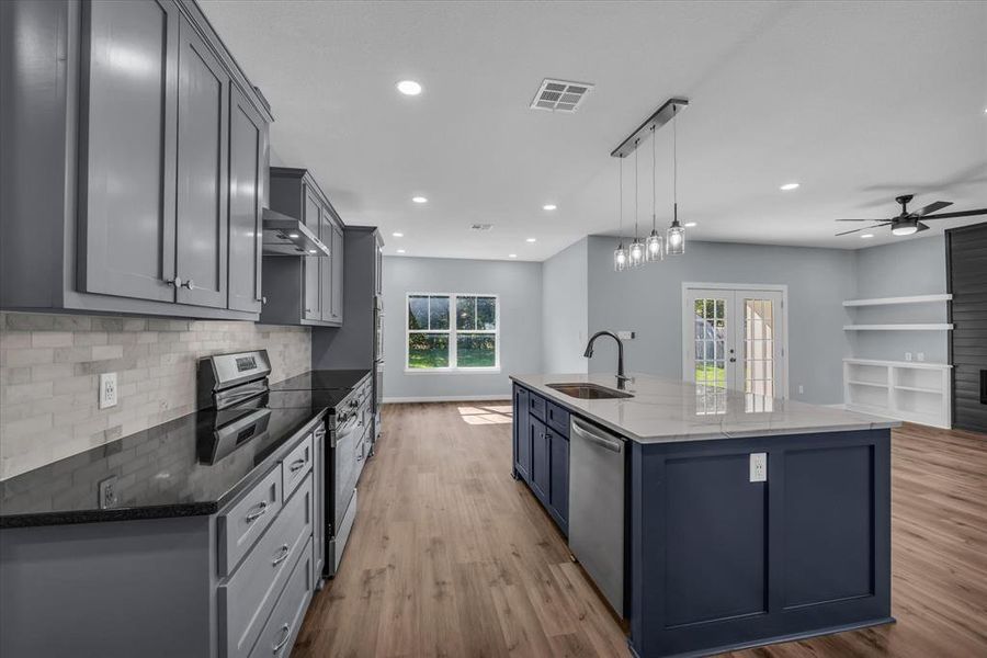 Kitchen with appliances with stainless steel finishes, dark stone countertops, decorative light fixtures, a large island with sink, and gray cabinets Kitchen with appliances with stainless steel finishes, dark stone countertops, decorative light fixtures, a large island with sink, and gray cabinets
