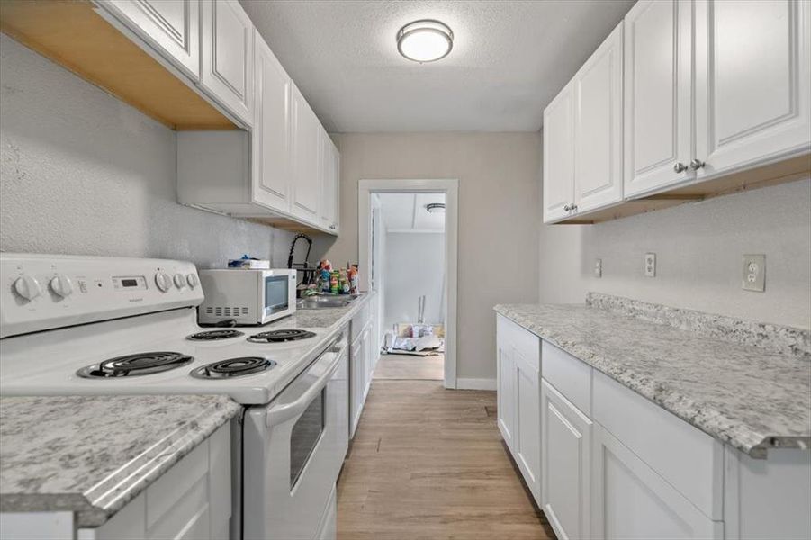 Kitchen with a textured ceiling, white appliances, light hardwood / wood-style floors, and white cabinetry Kitchen with a textured ceiling, white appliances, light hardwood / wood-style floors, and white cabinetry