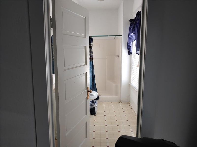 Bathroom featuring a walk-in shower, patterned tile-finish flooring, a window with blinds, and a paneled door Bathroom featuring a walk-in shower, patterned tile-finish flooring, a window with blinds, and a paneled door