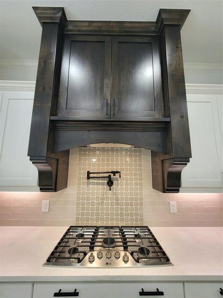 Kitchen featuring cooktop, backsplash, white cabinetry, and ornamental molding