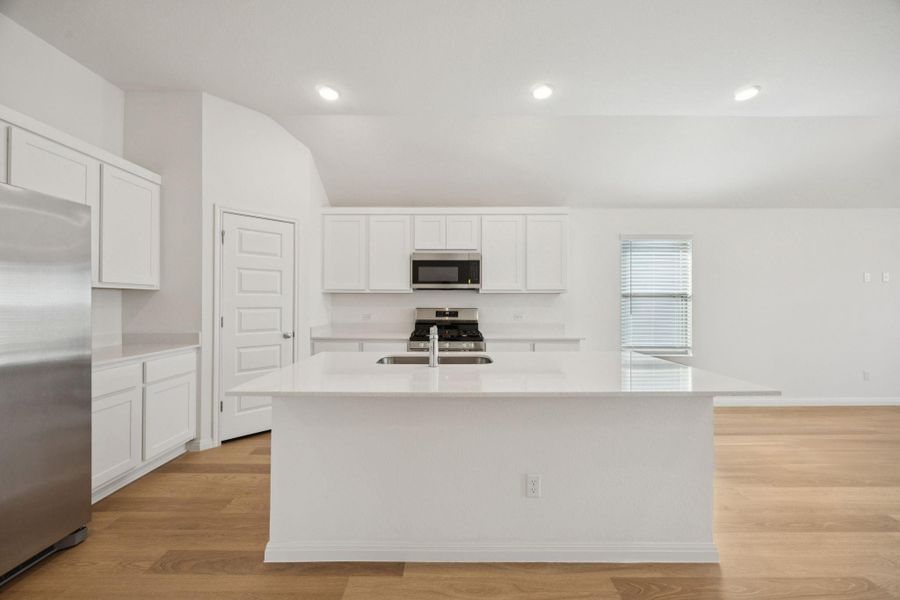 Kitchen with white cabinetry, light wood-style floors, appliances with stainless steel finishes, a center island with sink, and light stone countertops