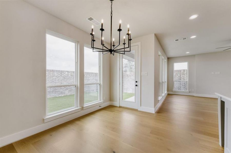 Expansive room featuring wood-finish flooring, a contemporary black chandelier, multiple floor-to-ceiling windows, and a glass-paned door