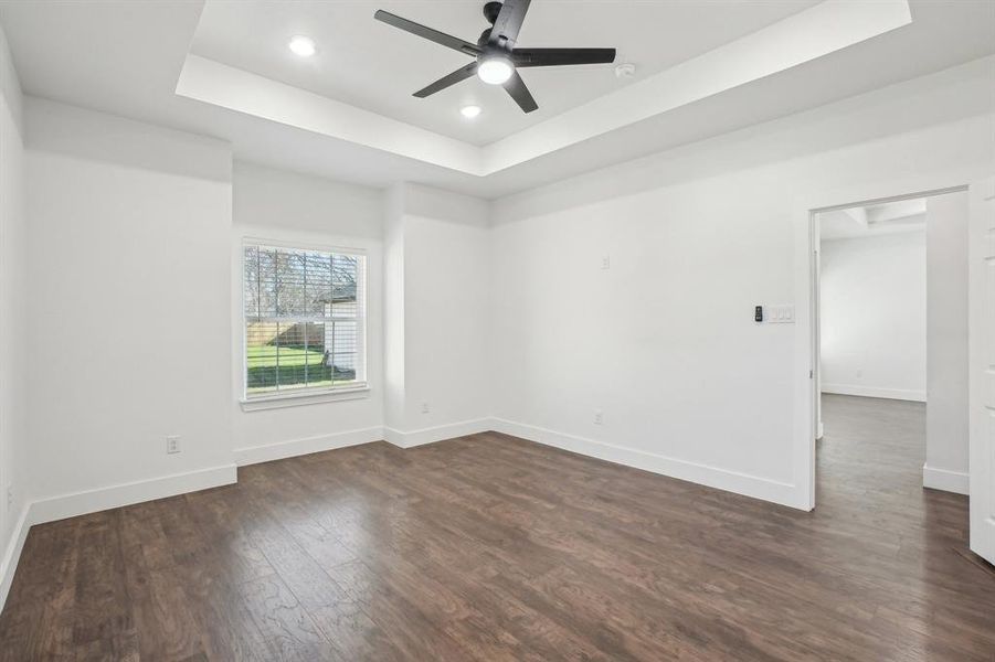 Primary bedroom with a tray ceiling, ceiling fan, and dark wood-type flooring