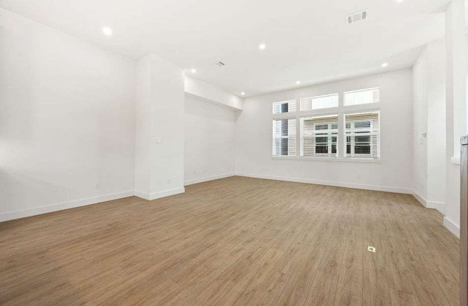 Bright and spacious living area with clean white walls, wide-plank wood-look floors, recessed lighting, and large windows that create an airy, modern feel. The room offers excellent wall space and an open footprint, making it easy to customize for entertaining, relaxing, or everyday living.