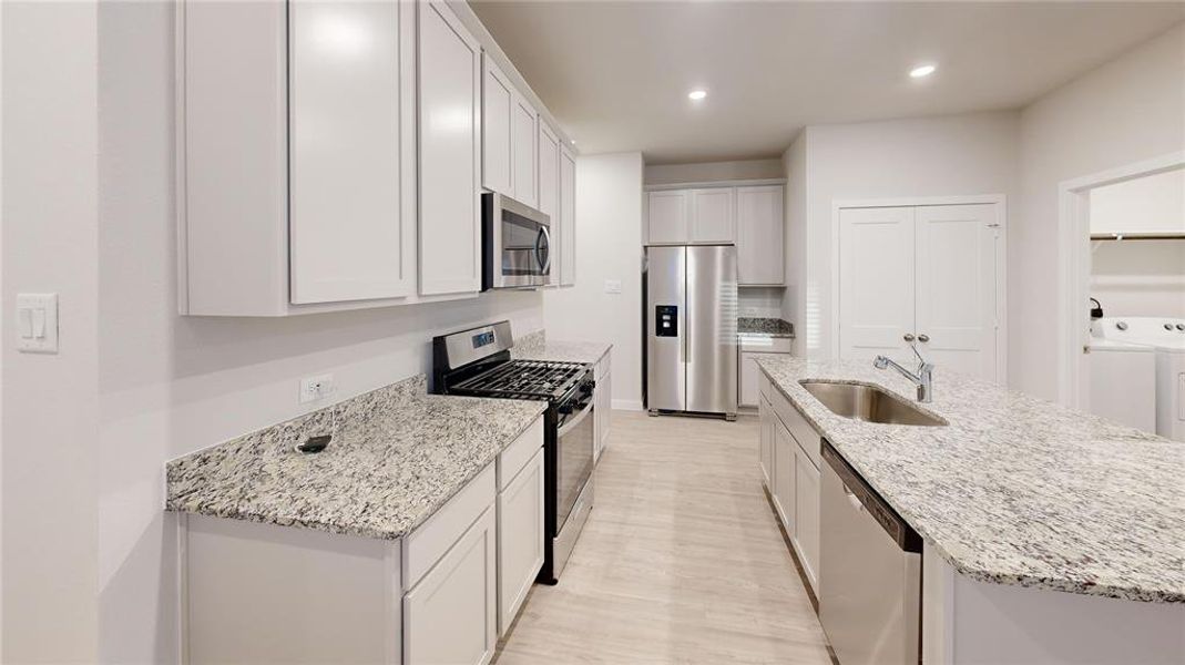 Modern kitchen with sleek granite countertops, stainless steel appliances, and ample cabinet space. Features an island with a sink, contemporary lighting, and a neutral color palette.