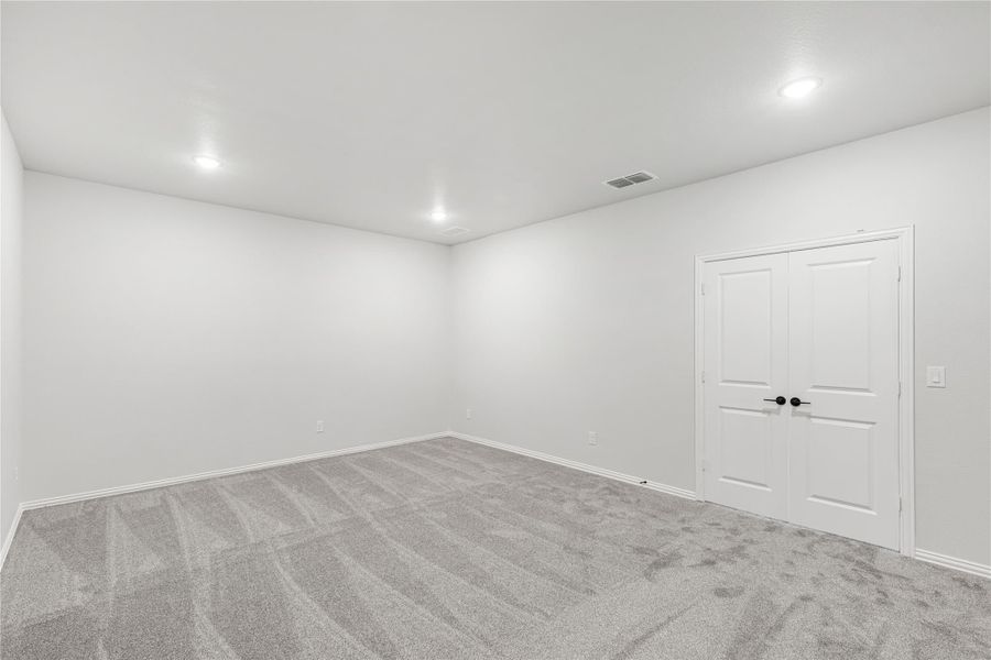 Empty bedroom with gray carpet, white walls, recessed lighting, and double closet doors