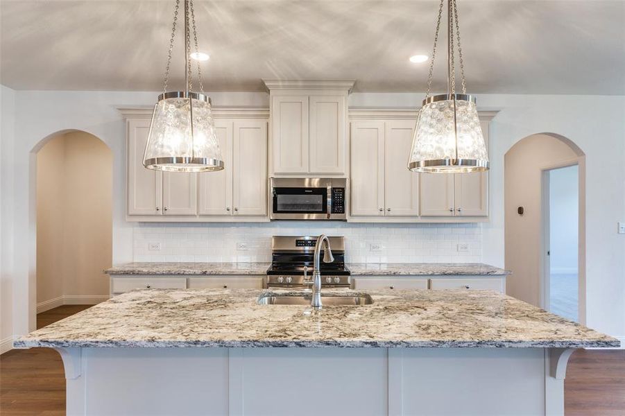 Kitchen featuring appliances with stainless steel finishes, decorative light fixtures, dark hardwood / wood-style flooring, sink, and a kitchen island with sink