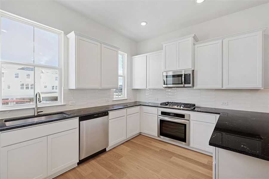 Kitchen featuring dark stone counters, white cabinetry, stainless steel appliances, light wood finished floors, and recessed lighting