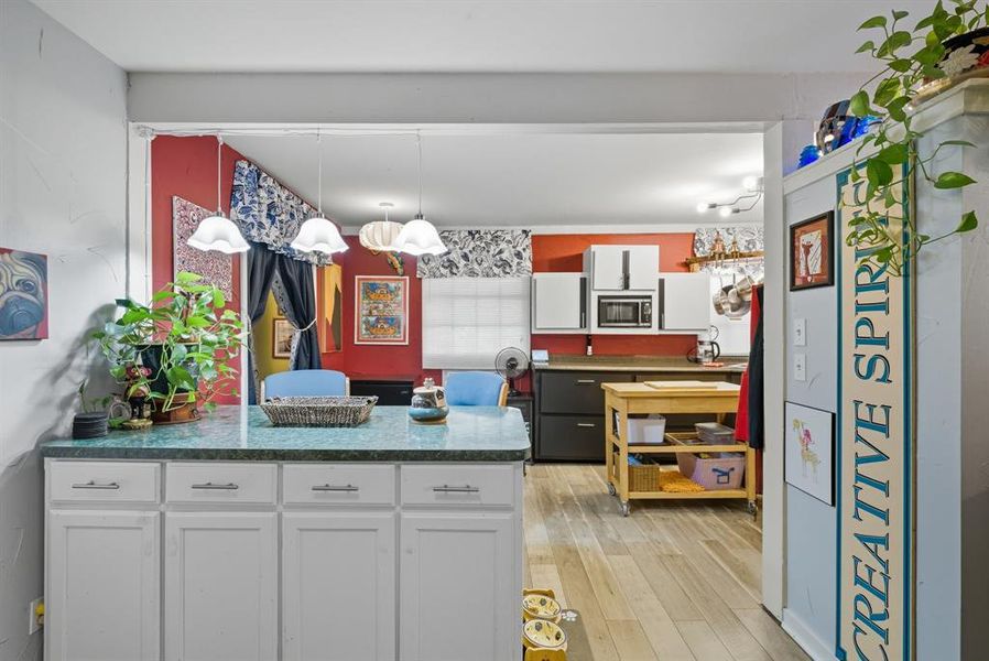 Kitchen with a peninsula, pendant lighting, white cabinetry, light wood-type flooring, and stainless steel microwave Kitchen with a peninsula, pendant lighting, white cabinetry, light wood-type flooring, and stainless steel microwave