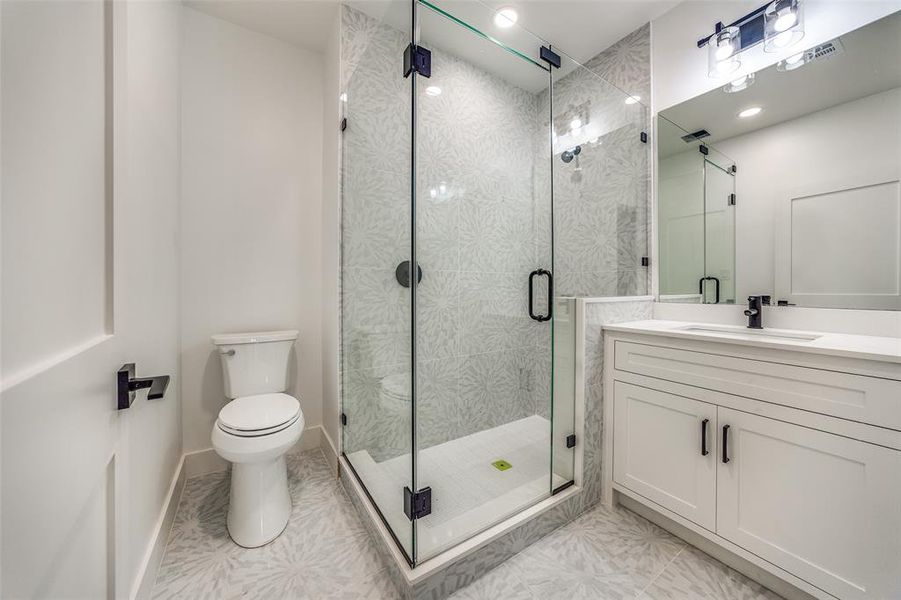 Bathroom featuring tile patterned flooring, vanity, toilet, and a shower with door