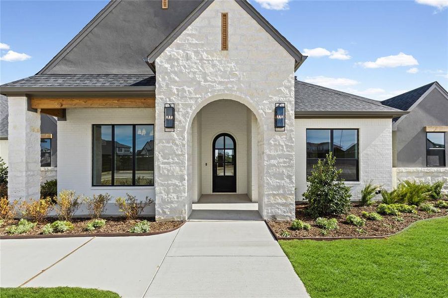 Doorway to property with a shingled roof, brick siding, and a yard