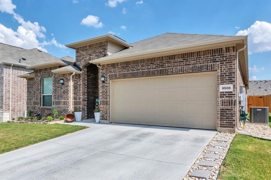 Single story home featuring brick siding, concrete driveway, an attached garage, a shingled roof, and a front yard