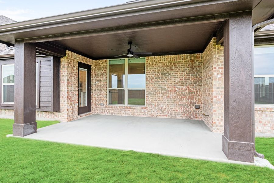 Covered back patio with ceiling fan, brick exterior, concrete floor, and green lawn