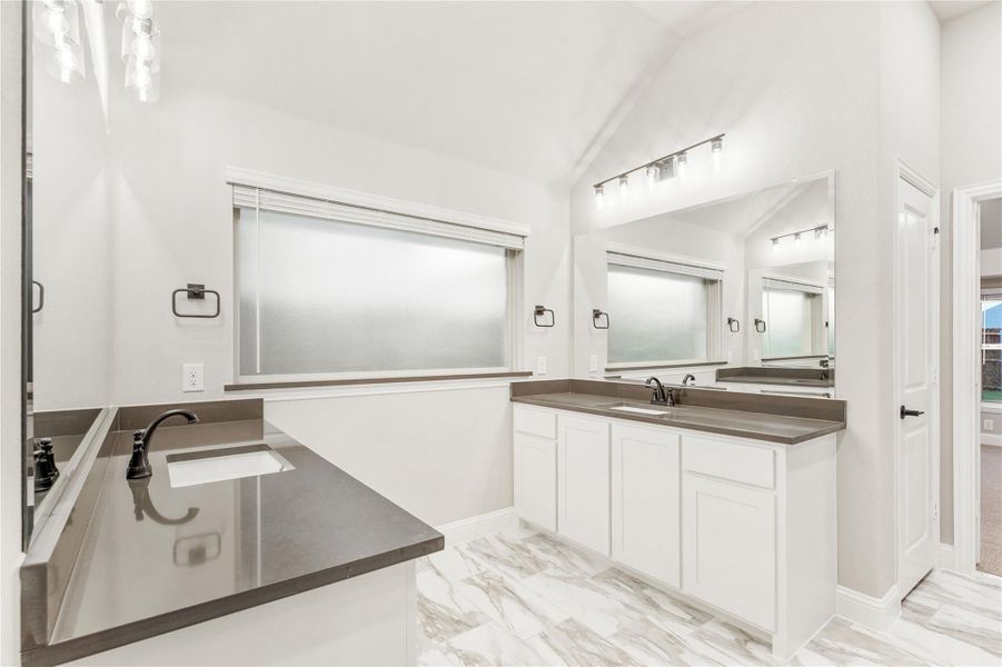 Master bathroom with dual vanities, white cabinets, dark countertops, and marble tile floors