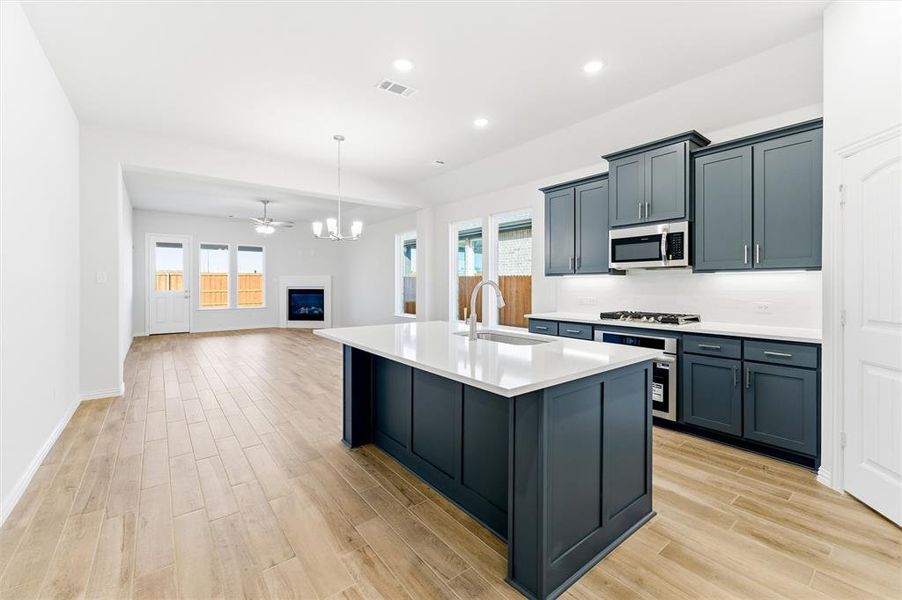 Kitchen with pendant lighting, a center island with sink, a fireplace, open floor plan, and light wood-style flooring