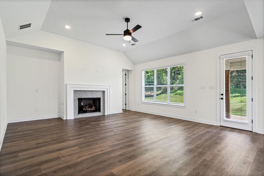 Spacious living area featuring wood-finish flooring, a vaulted ceiling, a fireplace with a white mantel and stone surround, recessed lighting, and a ceiling fan Spacious living area featuring wood-finish flooring, a vaulted ceiling, a fireplace with a white mantel and stone surround, recessed lighting, and a ceiling fan