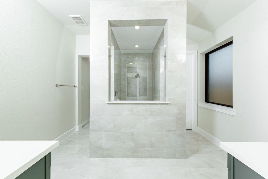 This stunningly updated primary bathroom is truly move-in ready! It features a large walk-in shower with tile surround, stained cabinetry with light countertops, dual vanities, mirrors, a generous walk-in closet with built-in shelving, soaring ceilings, custom paint, and sleek modern fixtures.