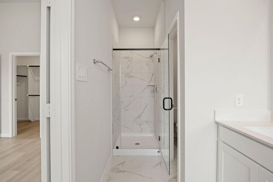 The primary bathroom features a modern, spa-inspired, glass-enclosed walk-in shower with a sleek, frameless black door and hardware. The shower is finished with elegant white marble-look tile, which extends onto the floor of the room. The primary bathroom features a modern, spa-inspired, glass-enclosed walk-in shower with a sleek, frameless black door and hardware. The shower is finished with elegant white marble-look tile, which extends onto the floor of the room.
