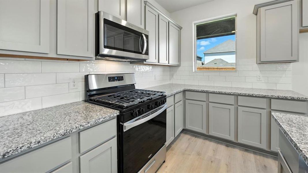 Kitchen featuring stainless steel appliances, gray cabinetry, light stone countertops, and backsplash