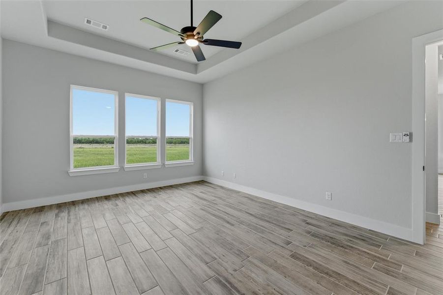 Spacious room featuring wood-finish flooring, a tray ceiling, and a ceiling fan