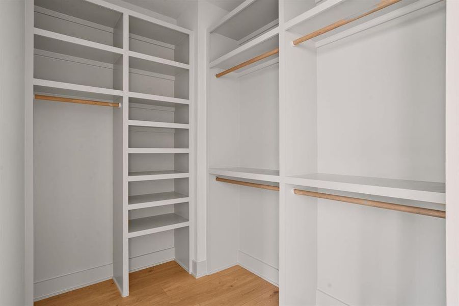 Custom closet system featuring white built-in shelving, multiple hanging rods, and wood-finish flooring