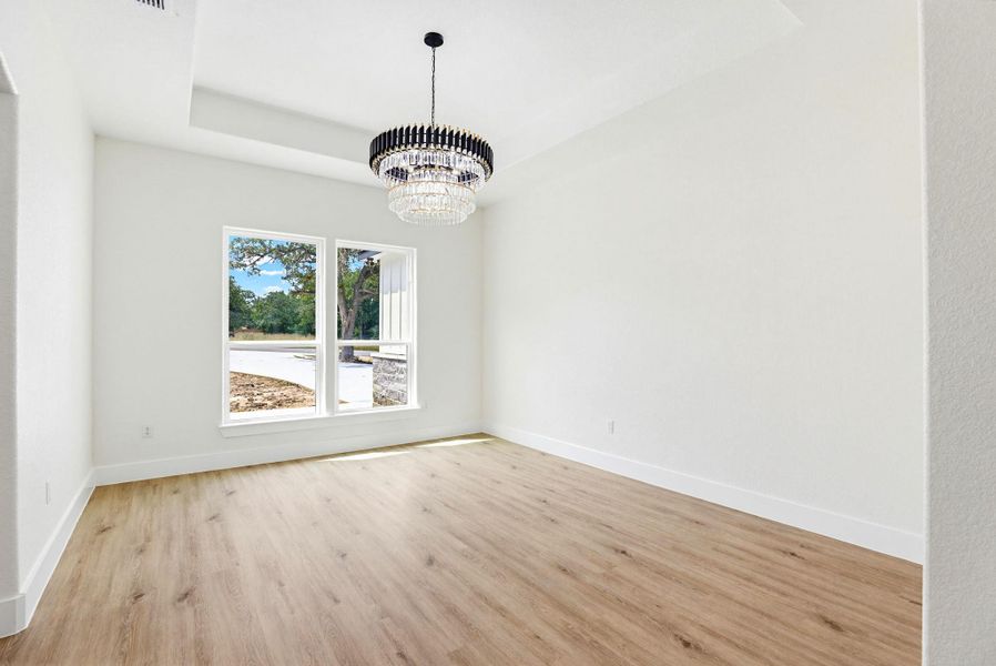 A spacious room with a contemporary chandelier and tray ceiling.