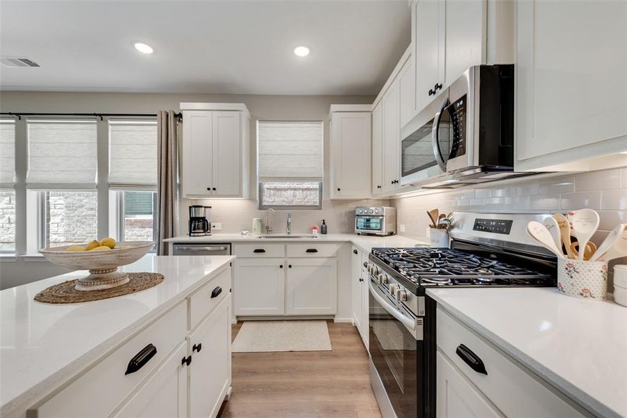 Kitchen featuring stainless steel appliances, white cabinets, light wood-style floors, backsplash, and recessed lighting