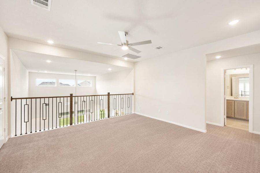 Open upstairs loft with carpet, ceiling fan, decorative iron railing, and view into bathroom Open upstairs loft with carpet, ceiling fan, decorative iron railing, and view into bathroom
