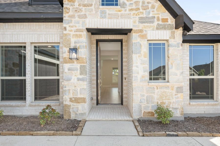 Home entrance with stone and brick exterior, black-framed front door, wall lantern, and brick walkway Home entrance with stone and brick exterior, black-framed front door, wall lantern, and brick walkway