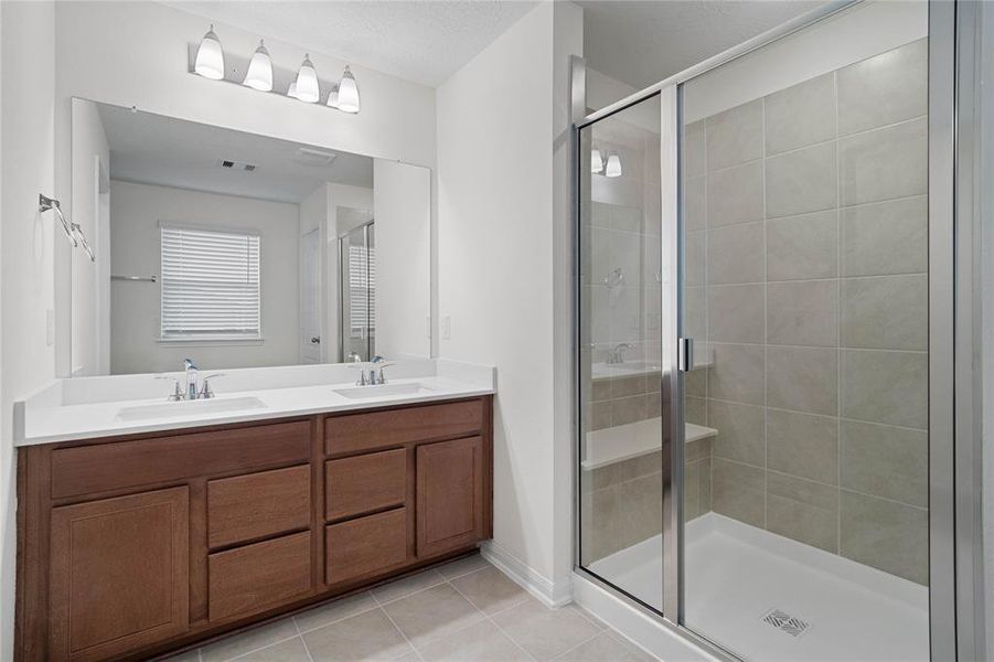 This primary bathroom is definitely move-in ready! Featuring an oversized walk-in shower with tile surround, stained cabinets with light countertops, dual vanities, high ceilings, neutral paint, sleek and modern finishes.