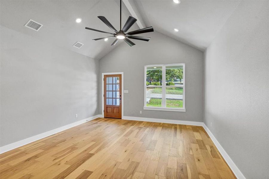 Empty room featuring light wood-style flooring, beamed ceiling, ceiling fan, and high vaulted ceiling