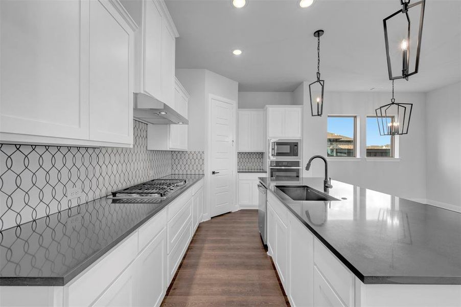 Kitchen featuring a spacious island, white cabinetry, dark wood-style floors, stainless steel appliances, and dark stone countertops Kitchen featuring a spacious island, white cabinetry, dark wood-style floors, stainless steel appliances, and dark stone countertops