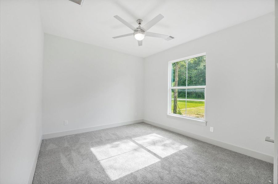 This is a bright, spacious room with a large window offering views of greenery. It features neutral walls, gray carpeting, and a modern ceiling fan. Perfect for a bedroom or office space. This is a bright, spacious room with a large window offering views of greenery. It features neutral walls, gray carpeting, and a modern ceiling fan. Perfect for a bedroom or office space.