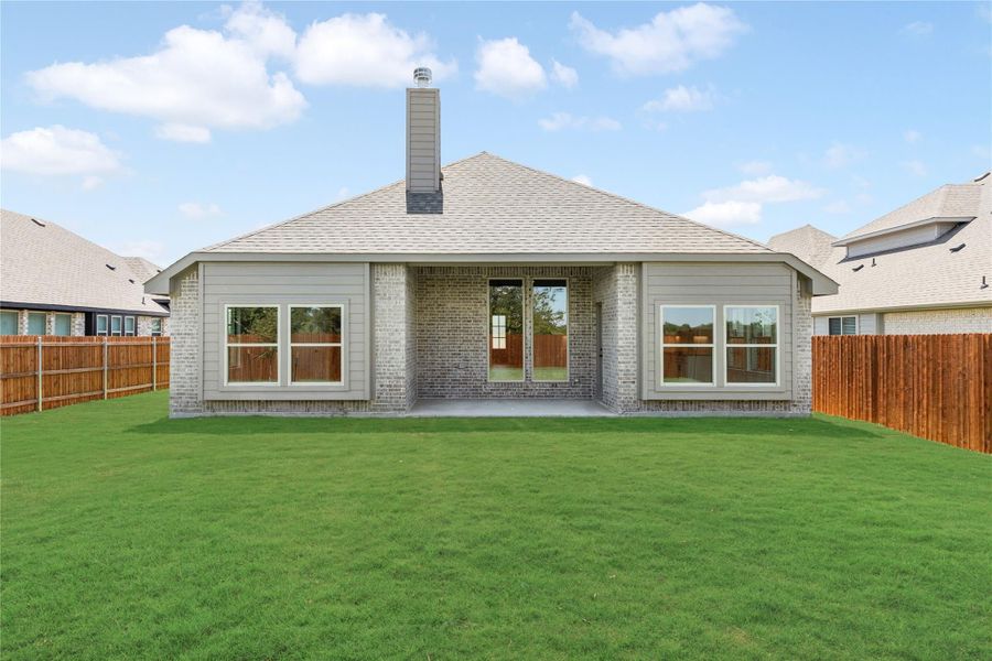 Rear exterior of brick home with covered patio, large fenced backyard, and chimney