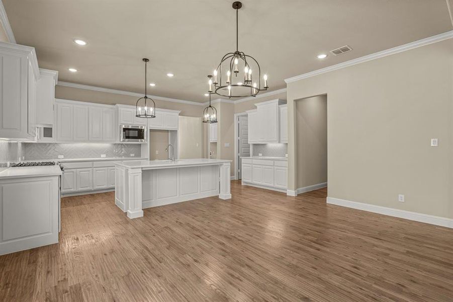 Kitchen featuring backsplash, white cabinetry, stainless steel microwave, light wood-type flooring, and a kitchen island with sink