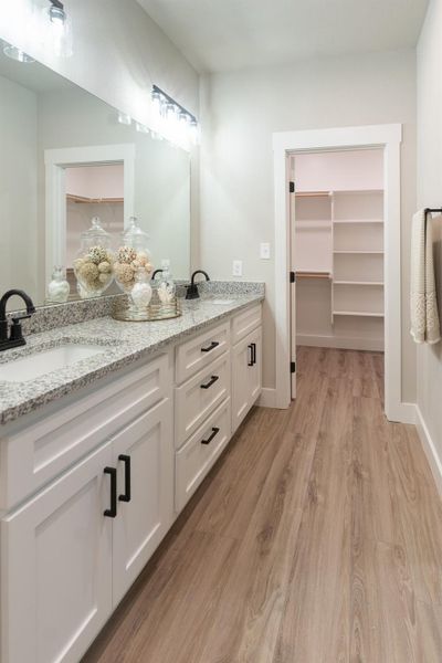 Bathroom with double vanity, wood finished floors, a walk in closet, and baseboards