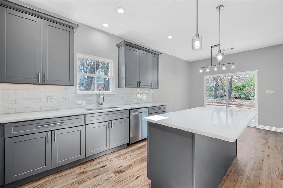 Kitchen with gray cabinetry, sink, light hardwood / wood-style flooring, stainless steel dishwasher, and tasteful backsplash