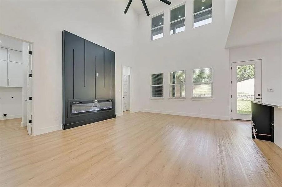 Vaulted ceiling living space featuring an electric fireplace with a black accent wall, wood-finish flooring, and multiple windows for abundant natural light