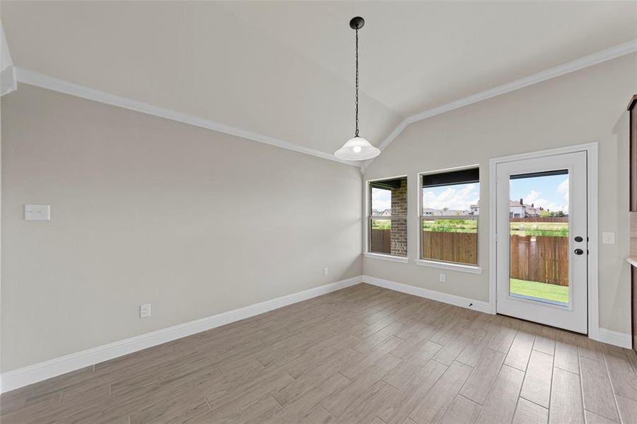 Unfurnished room with crown molding, light wood-style floors, and vaulted ceiling