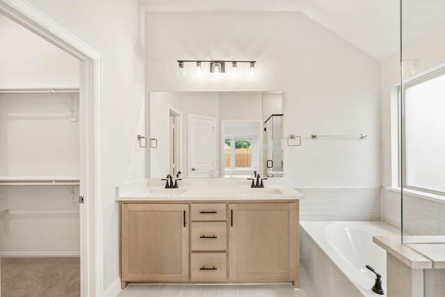 Master bathroom with double vanity, soaking tub, vaulted ceiling, and walk-in closet access