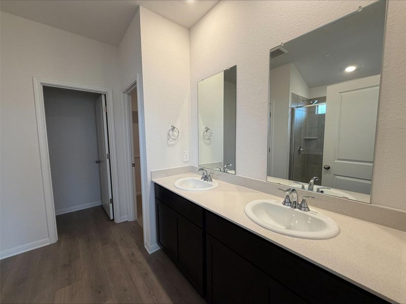 Bathroom featuring a shower stall, double vanity, and dark wood-style floors