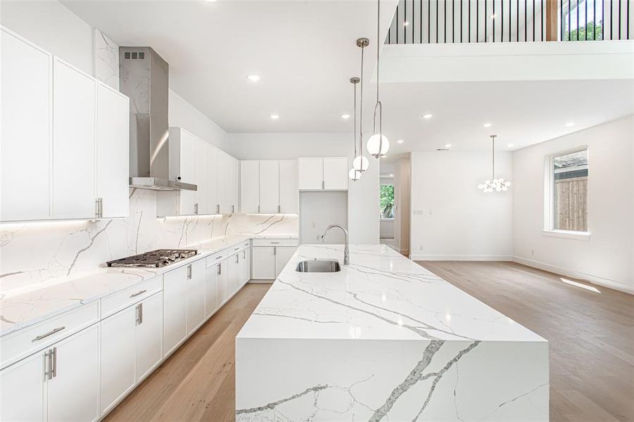 Kitchen featuring wall chimney range hood, a sink, stainless steel gas stovetop, light wood-type flooring, and plenty of natural light