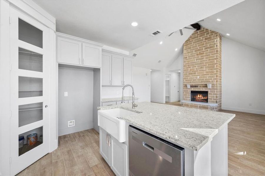 Kitchen with dishwasher, light hardwood / wood-style flooring, a center island with sink, and vaulted ceiling