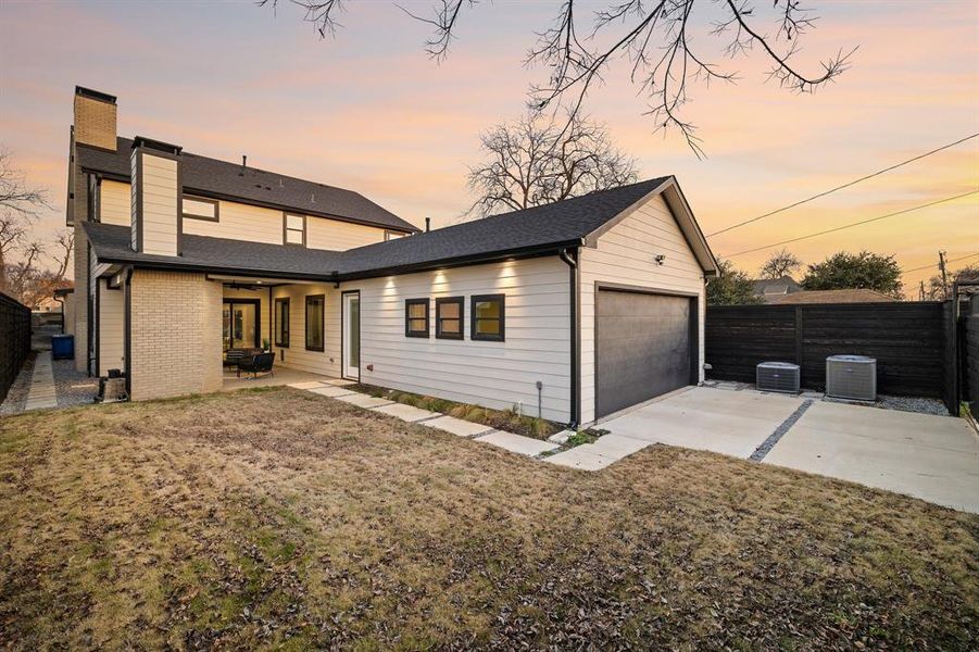 Back house at dusk featuring a patio, central AC, and a lawn