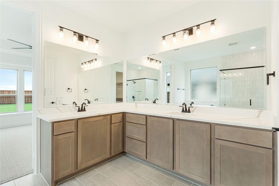 Master bathroom with L-shaped double vanity, wood cabinets, white countertops, and large mirrors above each sink.