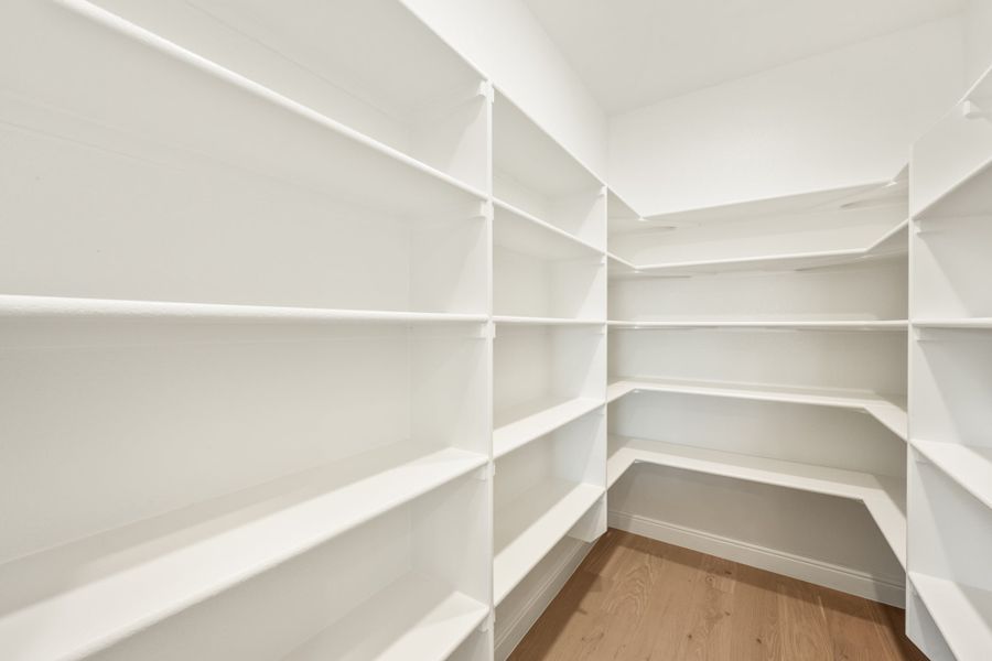 Walk-in pantry with floor-to-ceiling white shelving on three walls and hardwood floors